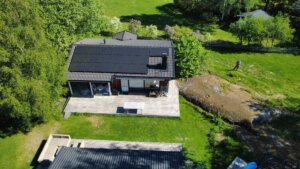 En skräddarsydd solcellsanläggning med svarta paneler monterad på ett villatak på Värmdö, fotograferad med drönare.