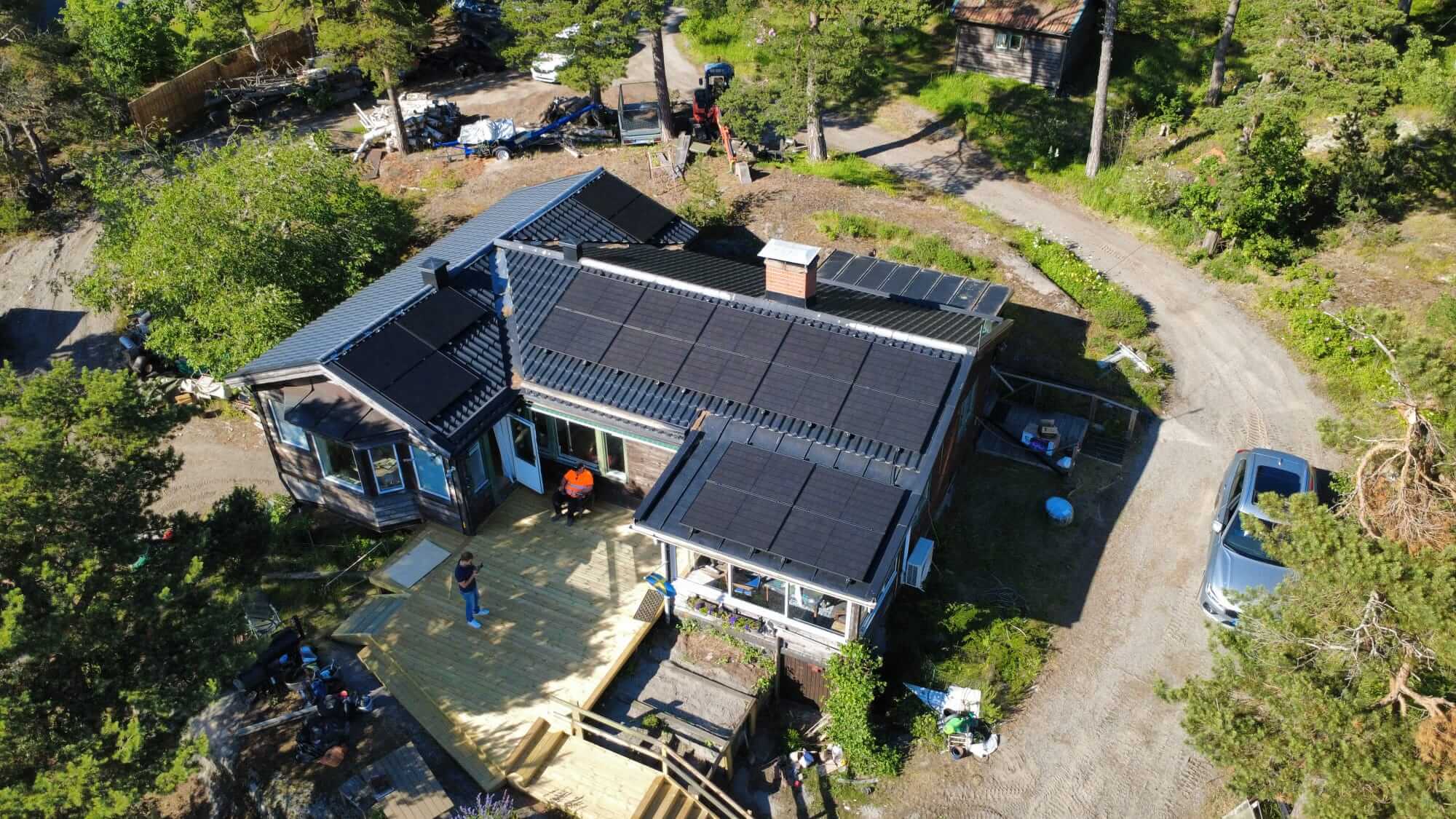 Solcellsanläggning på Ingarö Flygfoto över ett bostadhus i skärgårdsmiljö med 19 helsvarta solpaneler monterade i olika vinklar på taket.