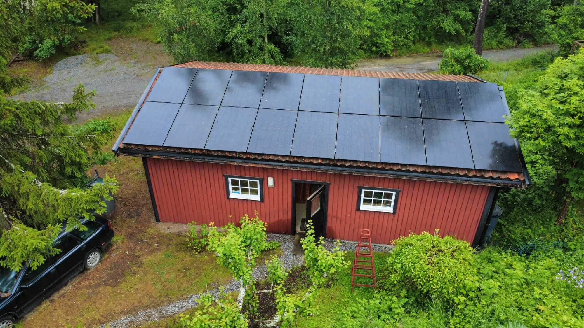 18 Astronergy glas-glas solpaneler monterade på rött tegeltak Drönarvy över en röd förrådsbyggnad på Norra Lagnö med 18 svarta solpaneler snyggt installerade på taket.
