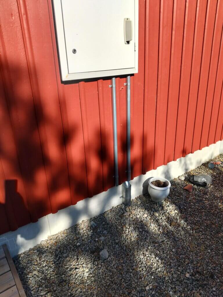 Nyinstallation av skyddsrör och kabeldragning upp till ett vitt fasadskåp på en röd träfasad.