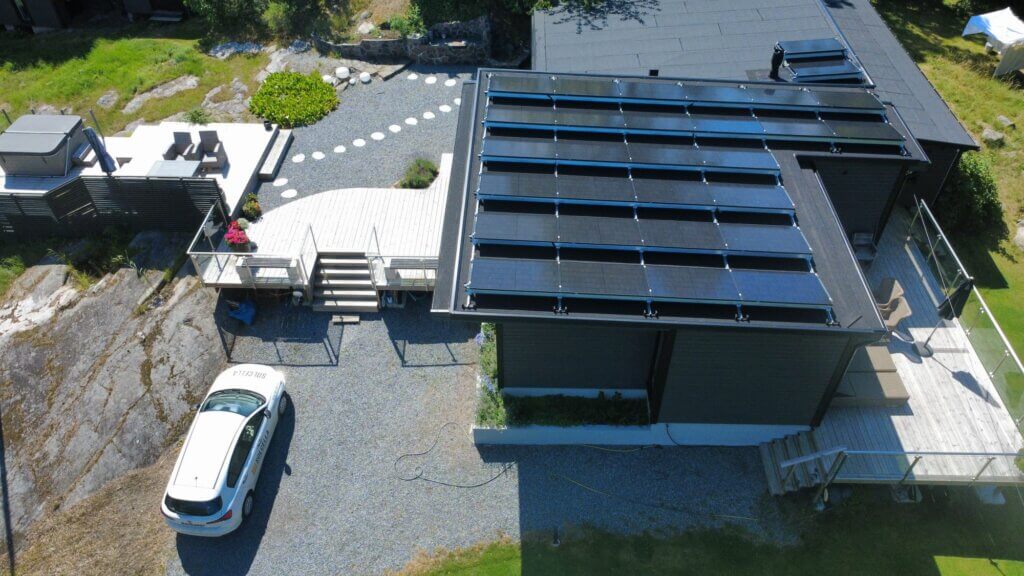 Solcellsanläggning på taket av en mörk träfasadvilla på Bullandö med Solcellas vita företagsbil parkerad på grusuppfarten.