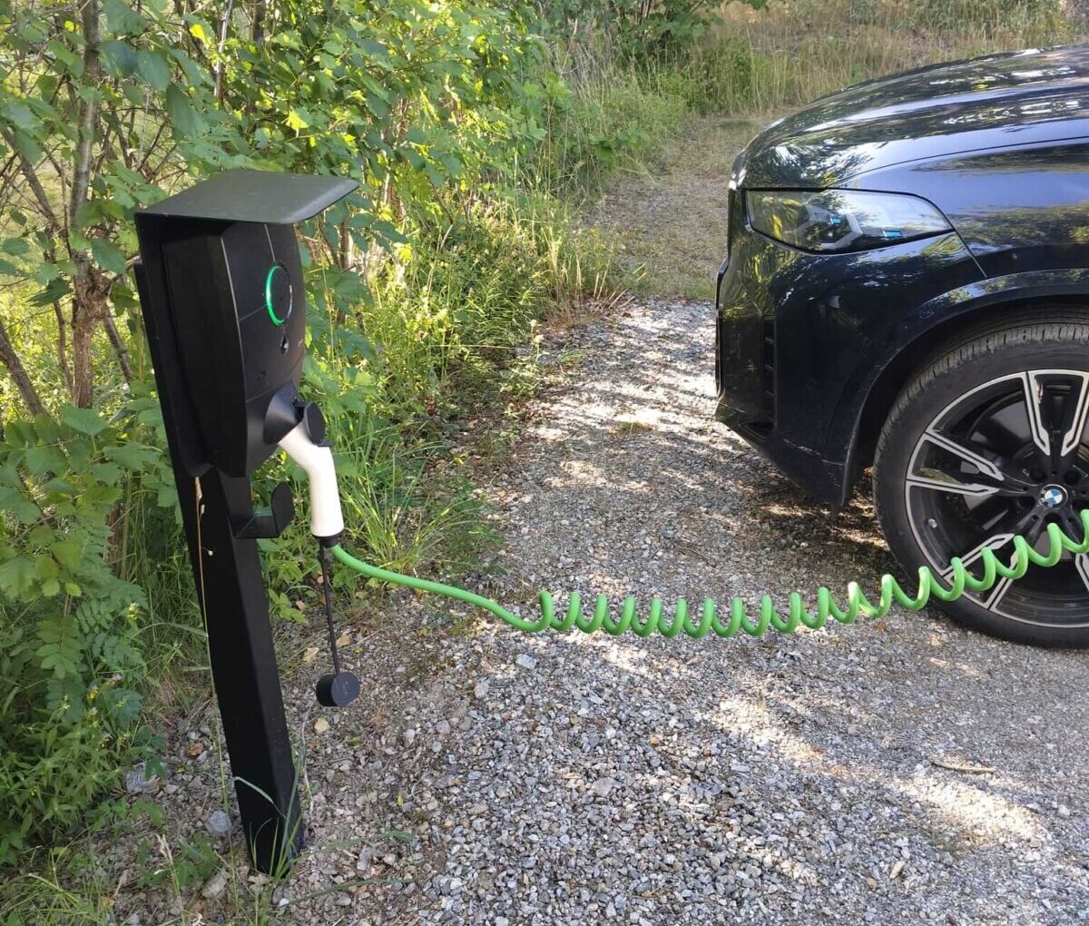 Grön kabel ansluten från en svart Zaptec laddstolpe till en parkerad elbil på Ingarö.