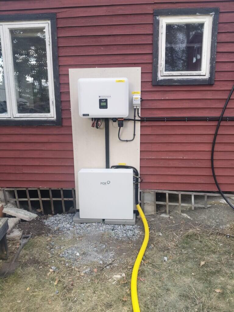 FoxESS EP12 utomhusbatteri och växelriktare snyggt installerat på fasaden till en röd sommarstuga på Bullandö