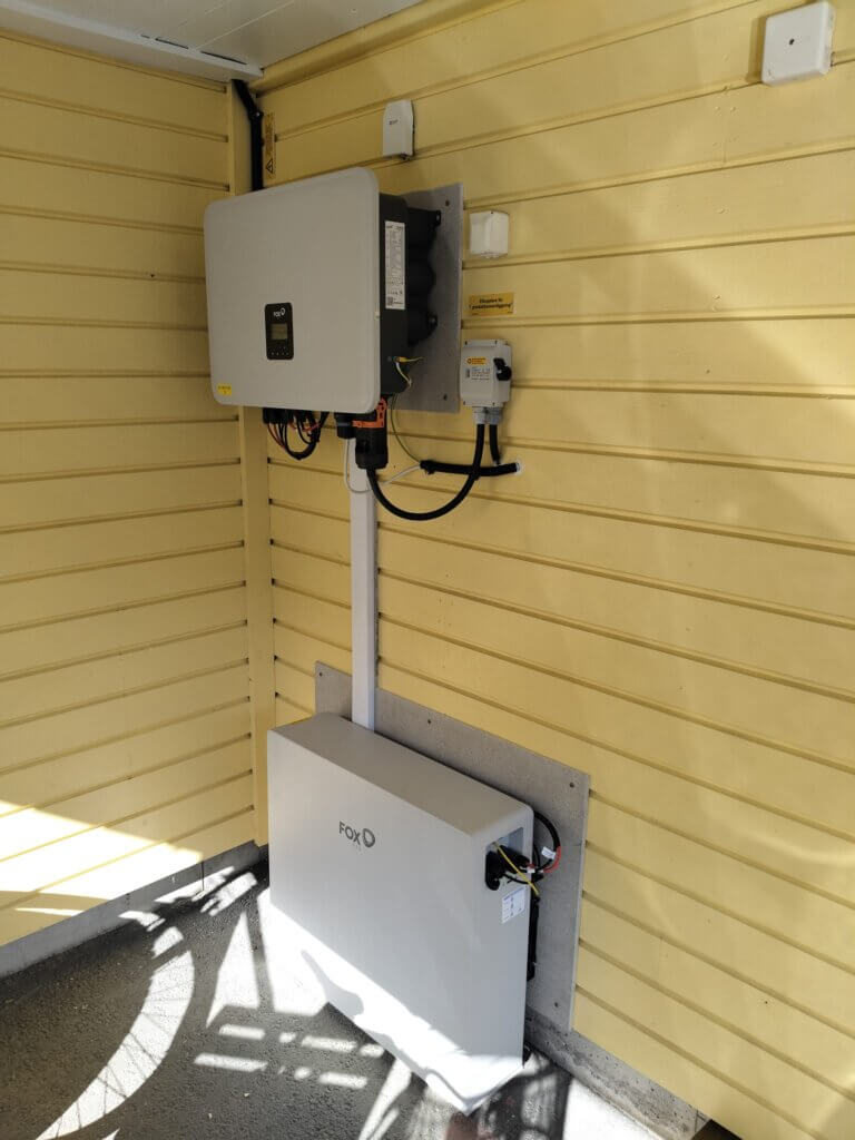 Väggmonterad FoxESS växelriktare och 11,5 kWh utomhusbatteri med värmeslinga installerat på fasad i Gustavsberg.