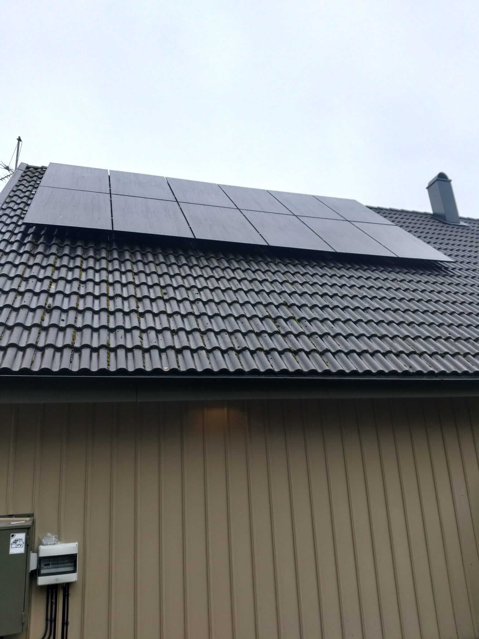 Två rader svarta solpaneler monterade på tak med betongpannor i Tullinge